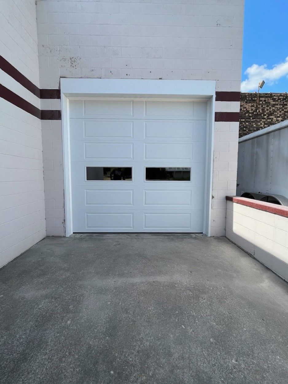 A white garage door with two windows on the side of a building.