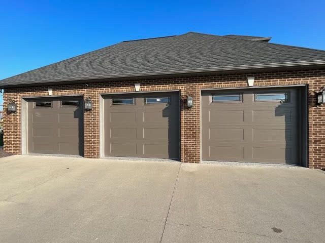 A brick house with three garage doors and a blue sky in the background.