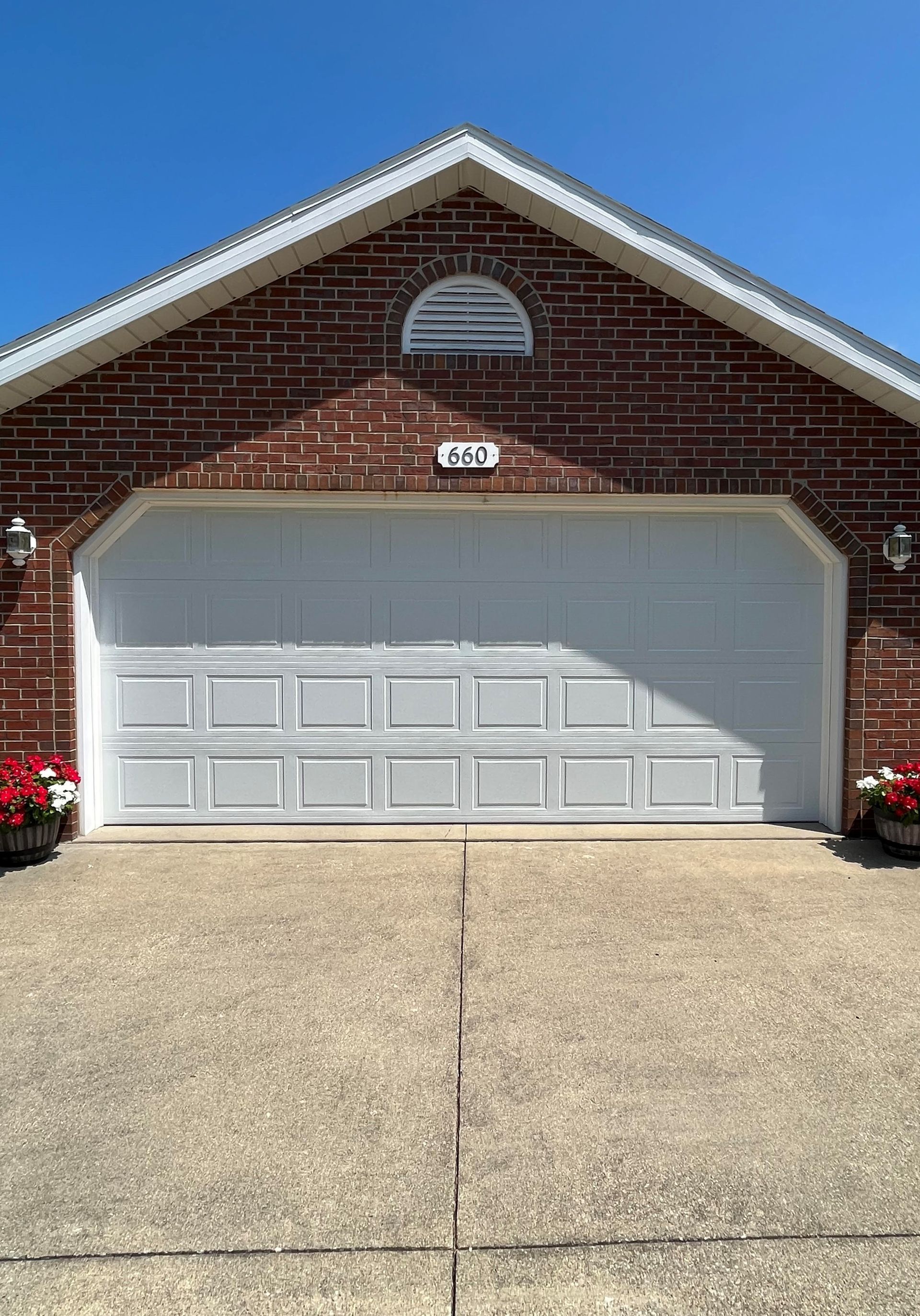 A brick house with a white garage door and flowers in front of it.