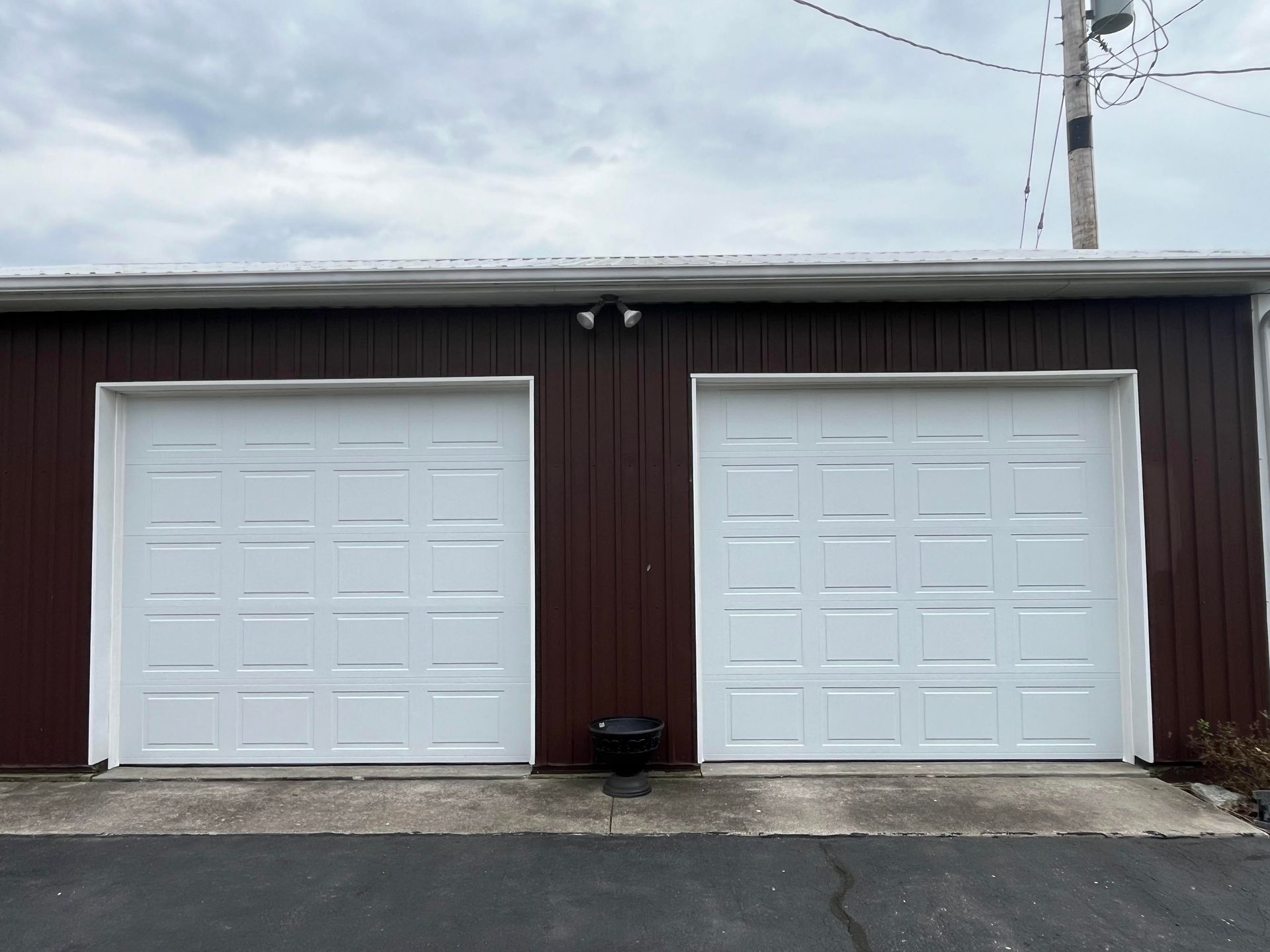 Two white garage doors are on a brown building.
