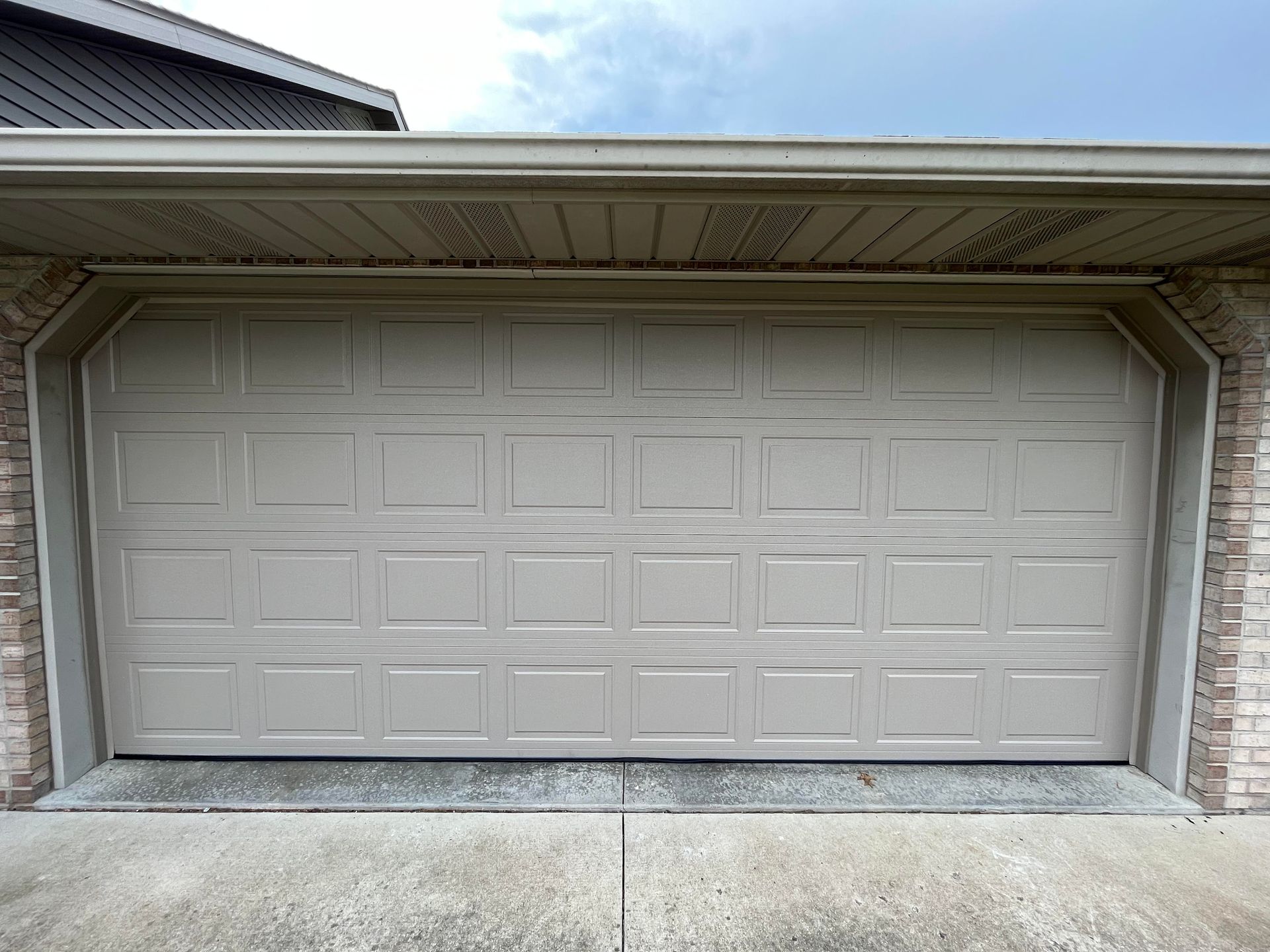A white garage door is open in front of a brick building.
