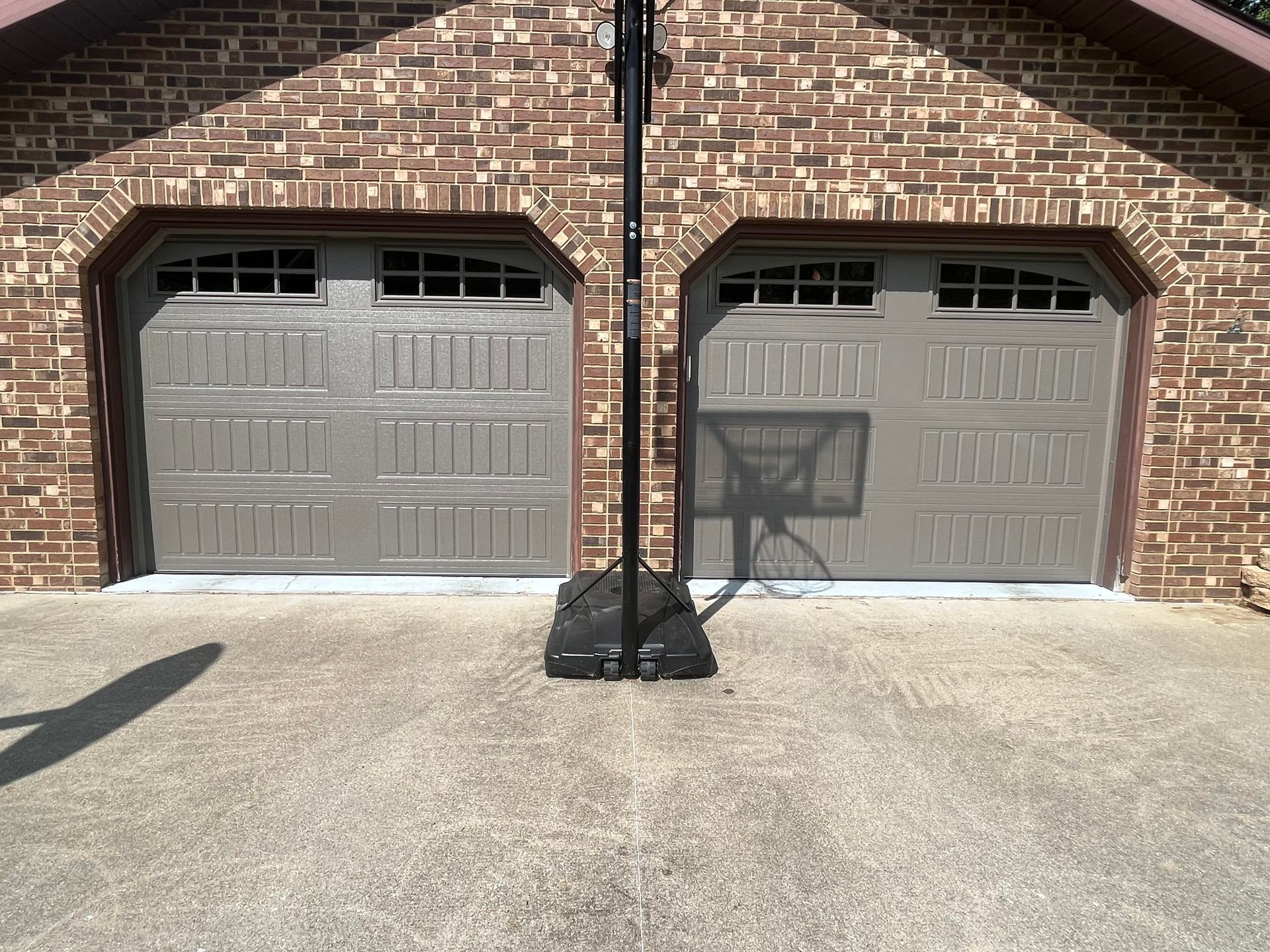 A basketball hoop is sitting in front of a brick garage door.