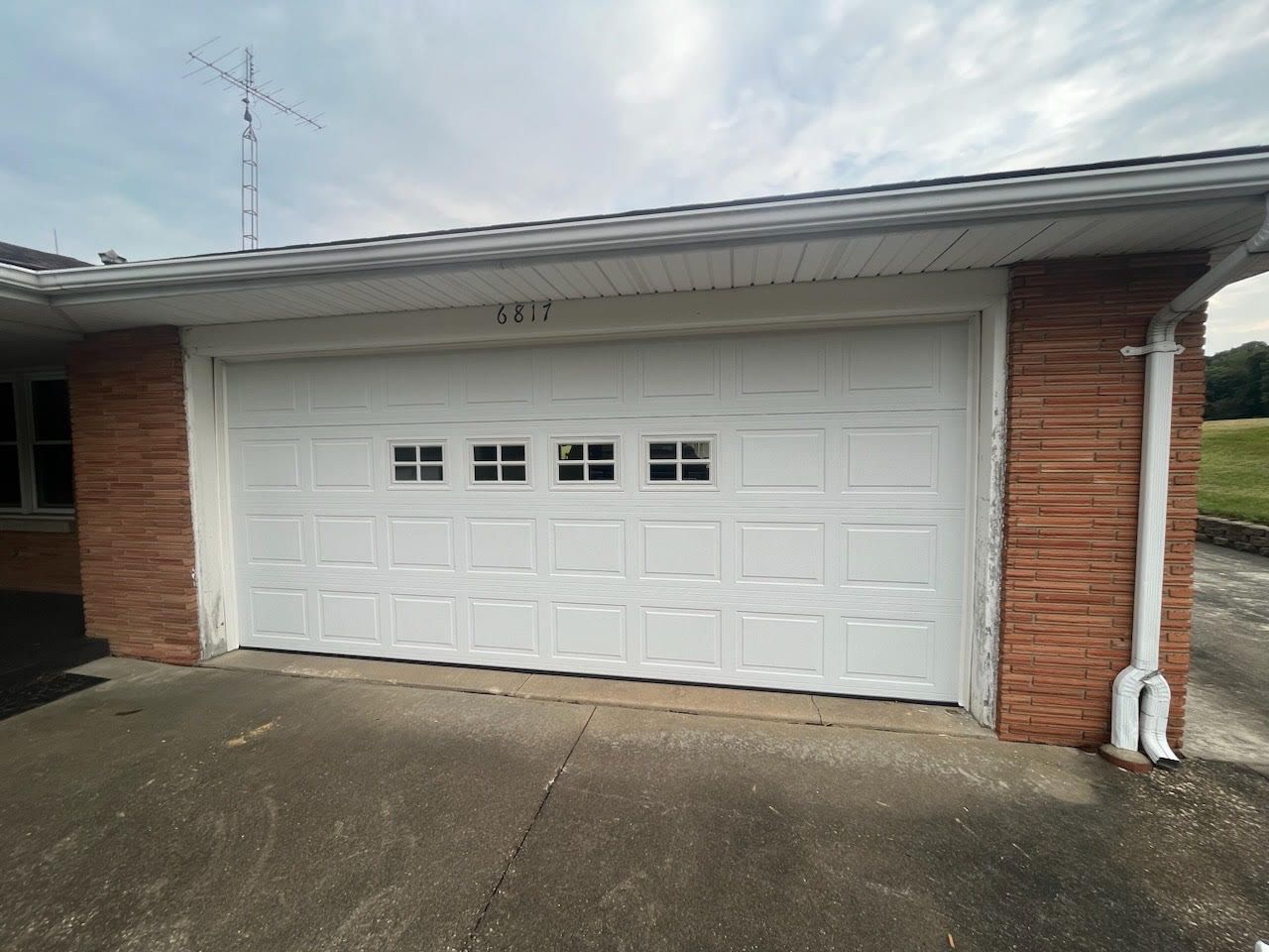 A white garage door is on the side of a brick house.