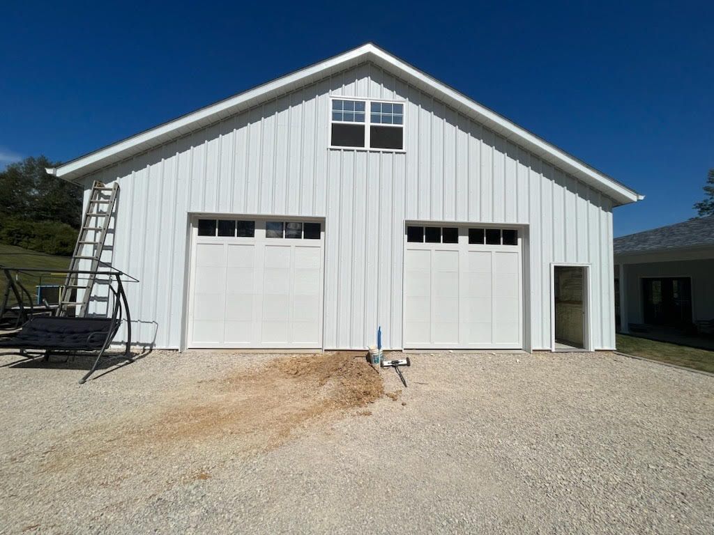 A white garage with two garage doors and a ladder in front of it.