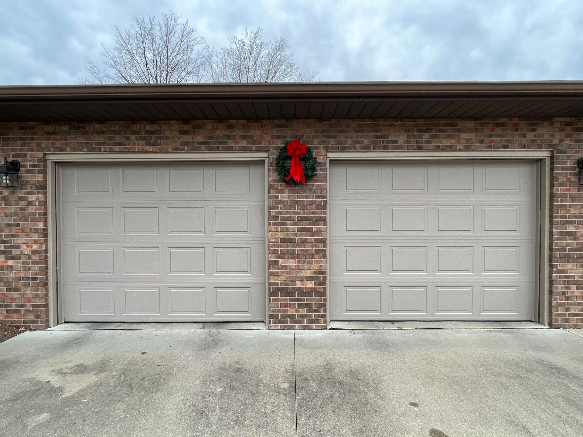 There is a christmas wreath on the garage door of a brick house.