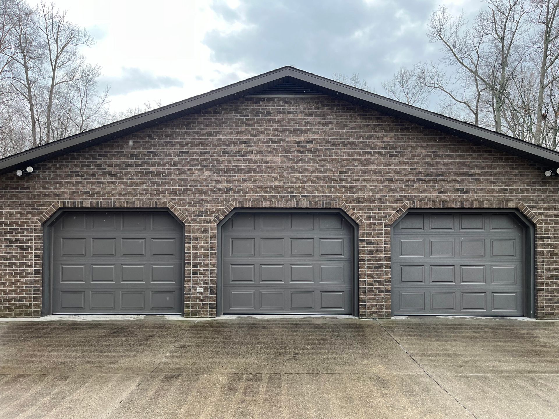 A brick garage with three garage doors on a cloudy day.