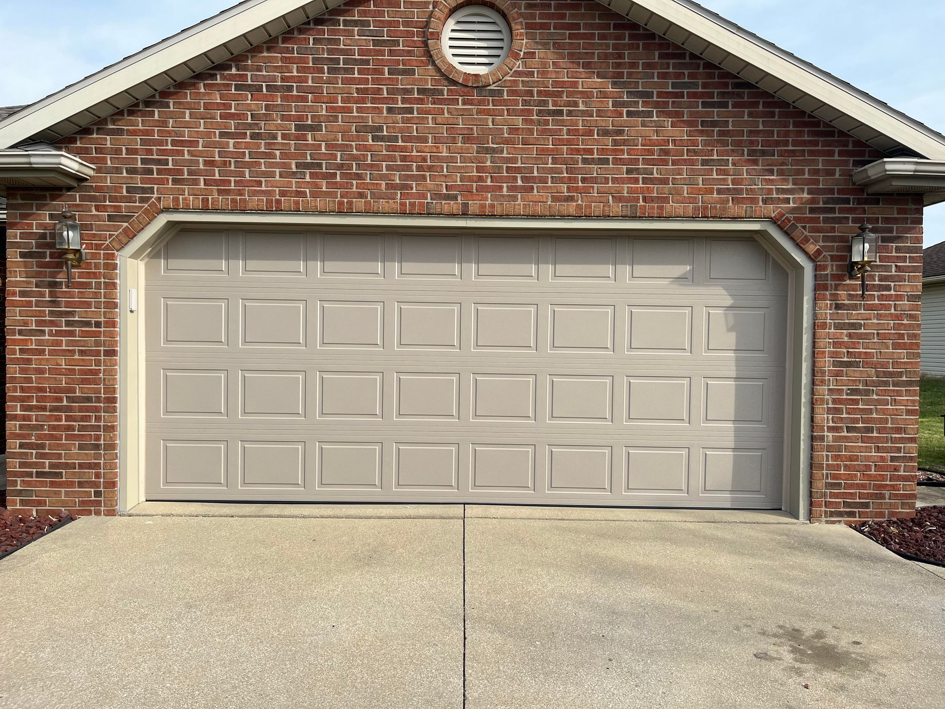 A brick house with a tan garage door and a concrete driveway.