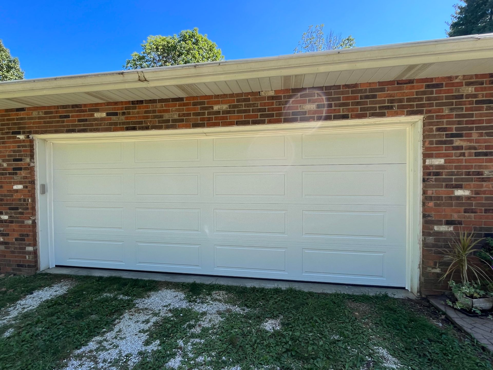 A white garage door is sitting in front of a brick house.