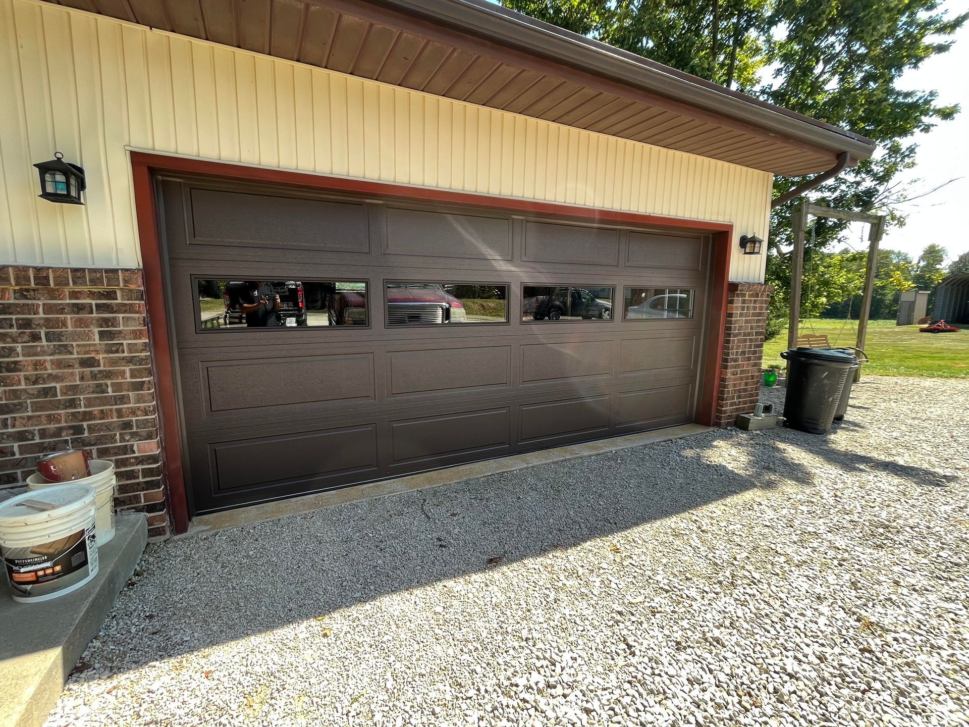 A brown garage door is sitting on top of a gravel driveway next to a brick building.