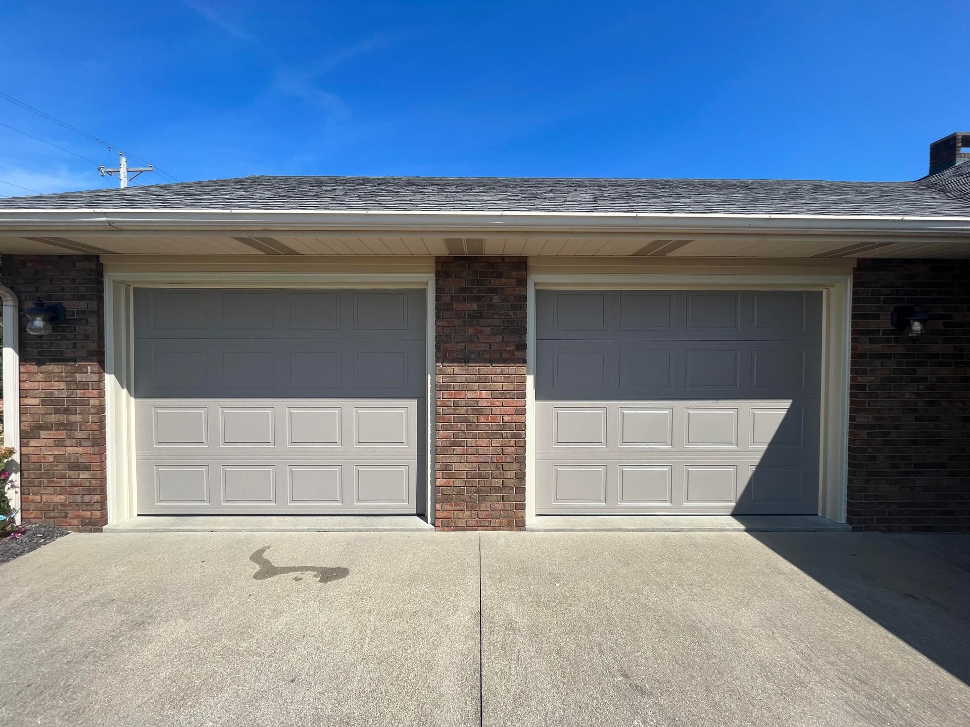 A brick house with two garage doors and a concrete driveway.