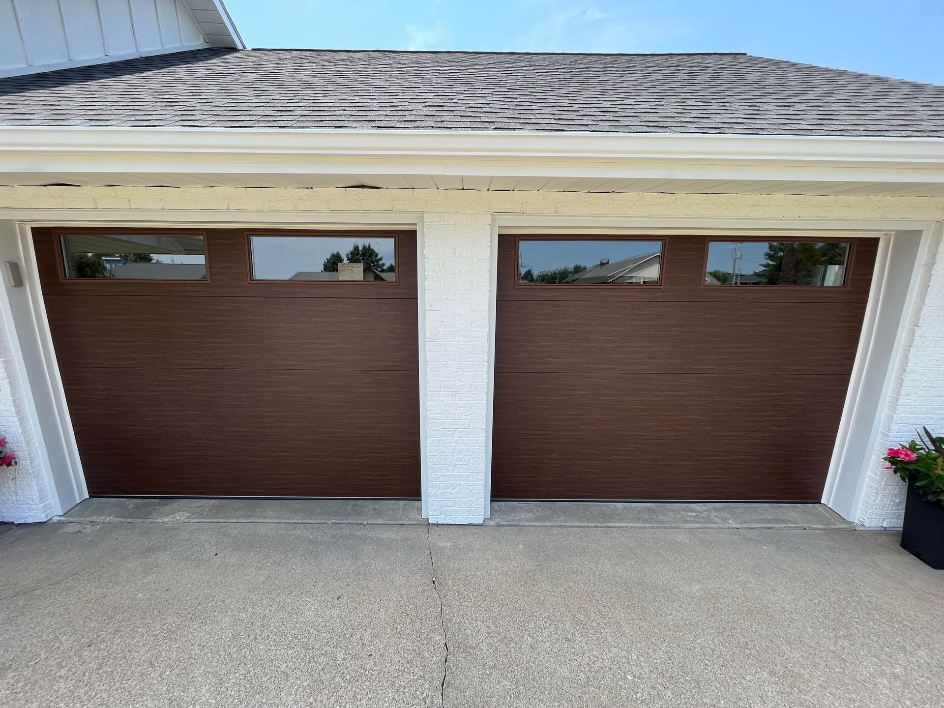 A white house with two brown garage doors and a roof.