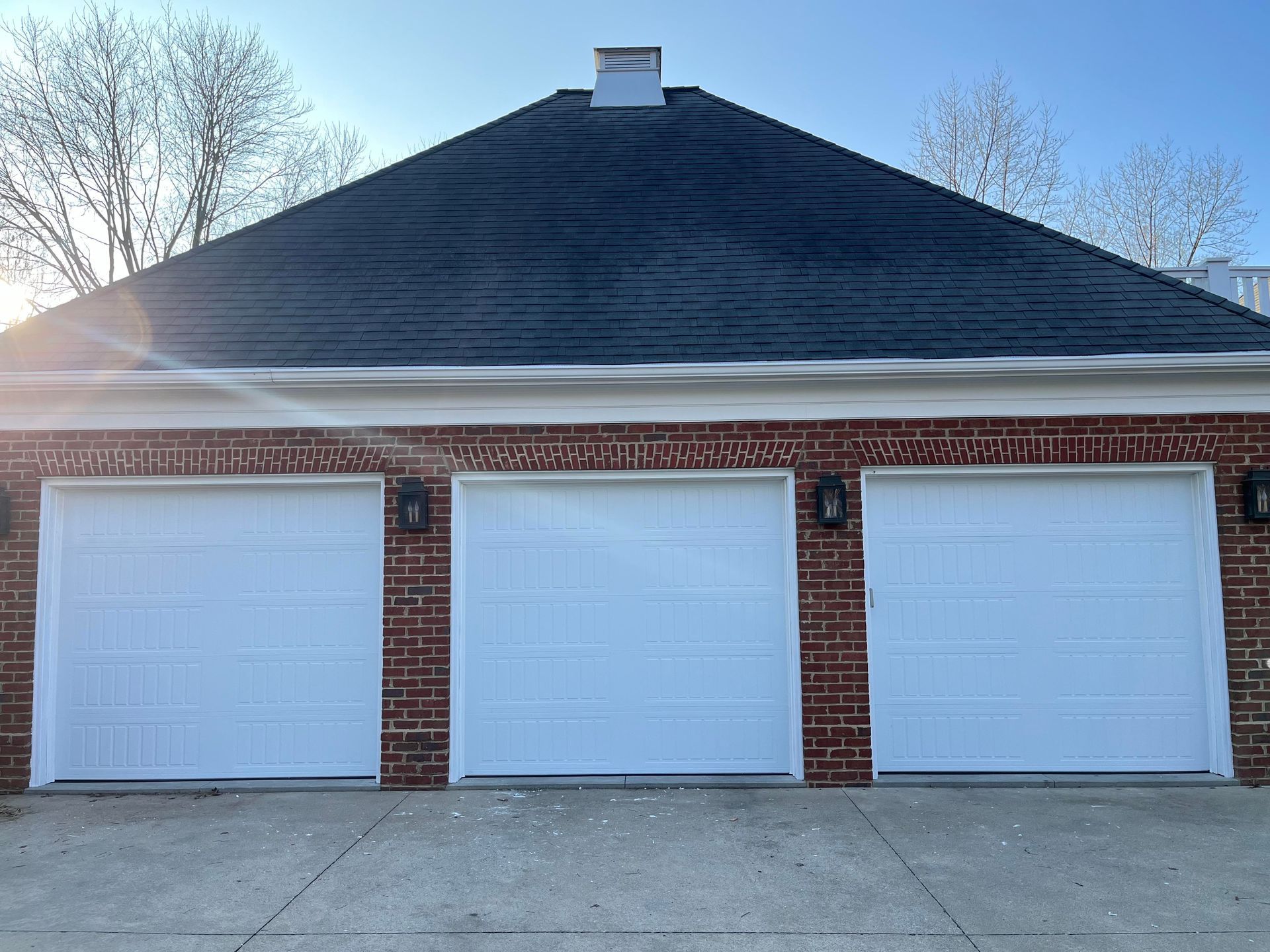 A brick garage with three white garage doors and a black roof.