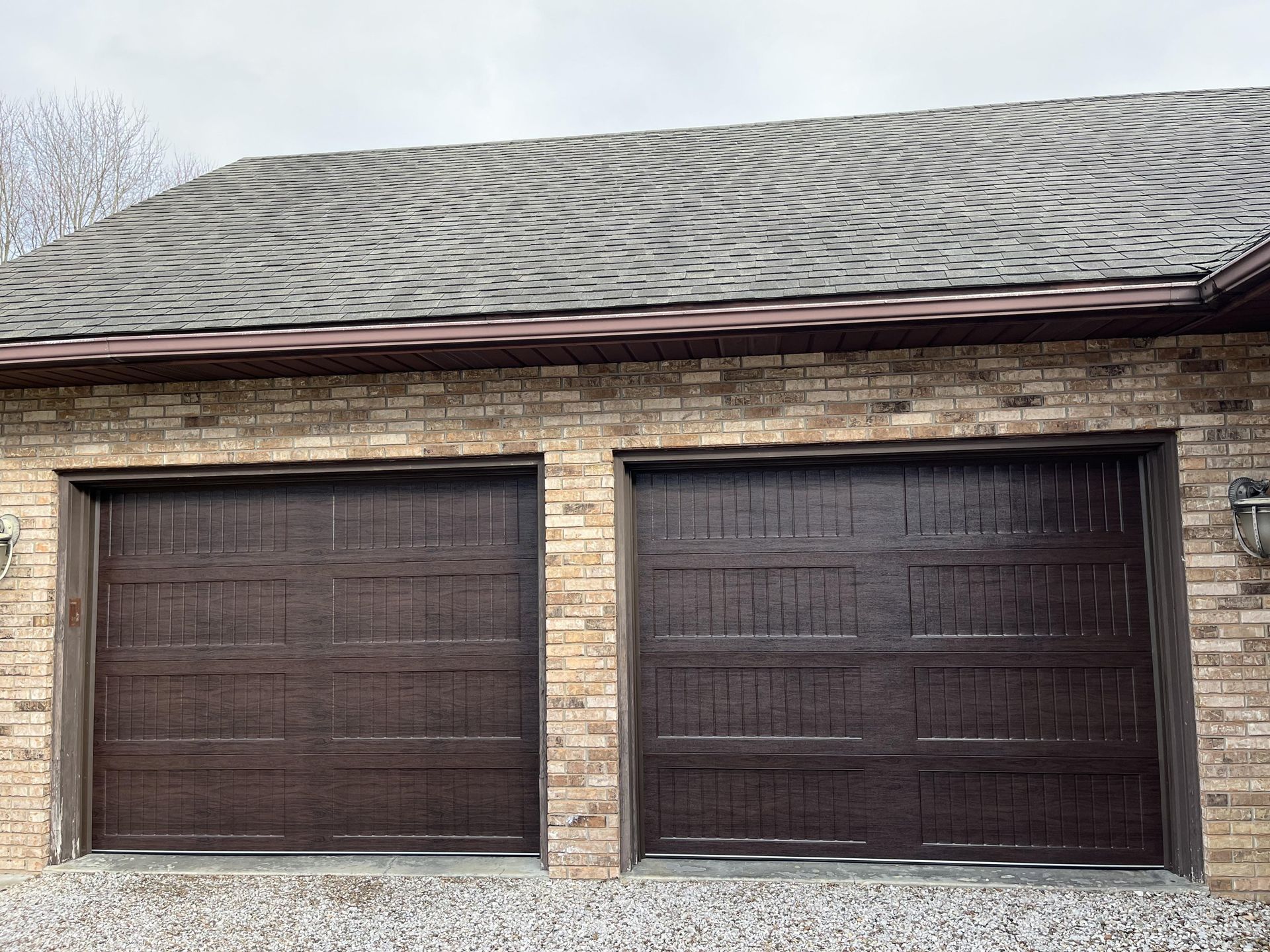 A brick garage with two brown garage doors and a gray roof.