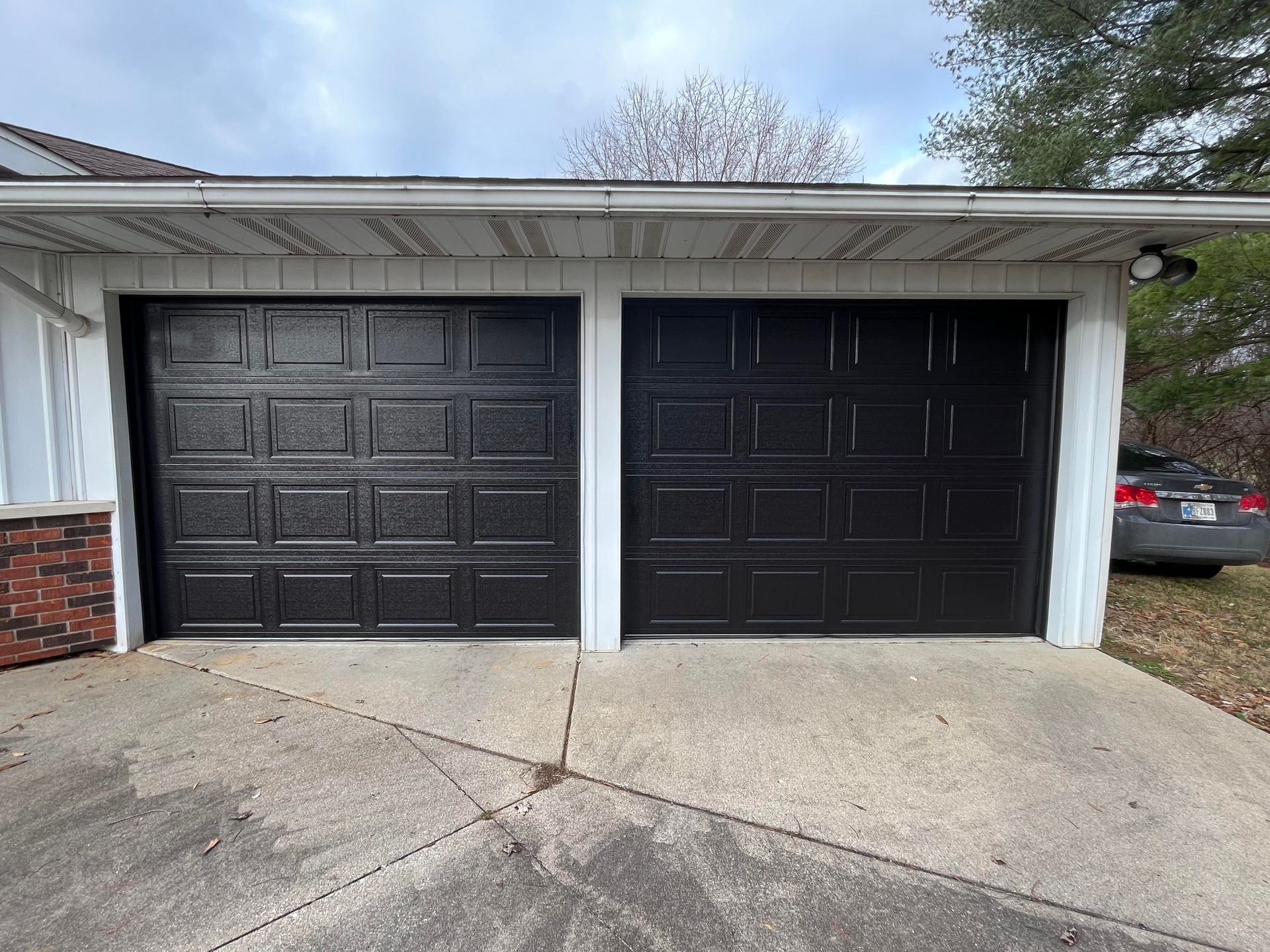 Two black garage doors are sitting next to each other in front of a house.