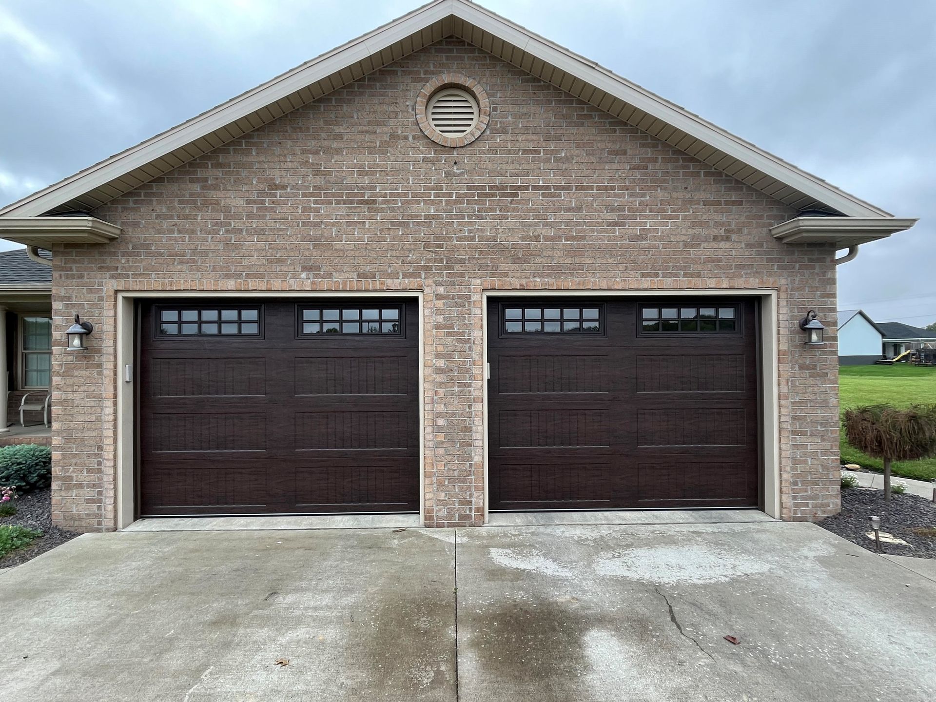A brick house with two brown garage doors and a concrete driveway.