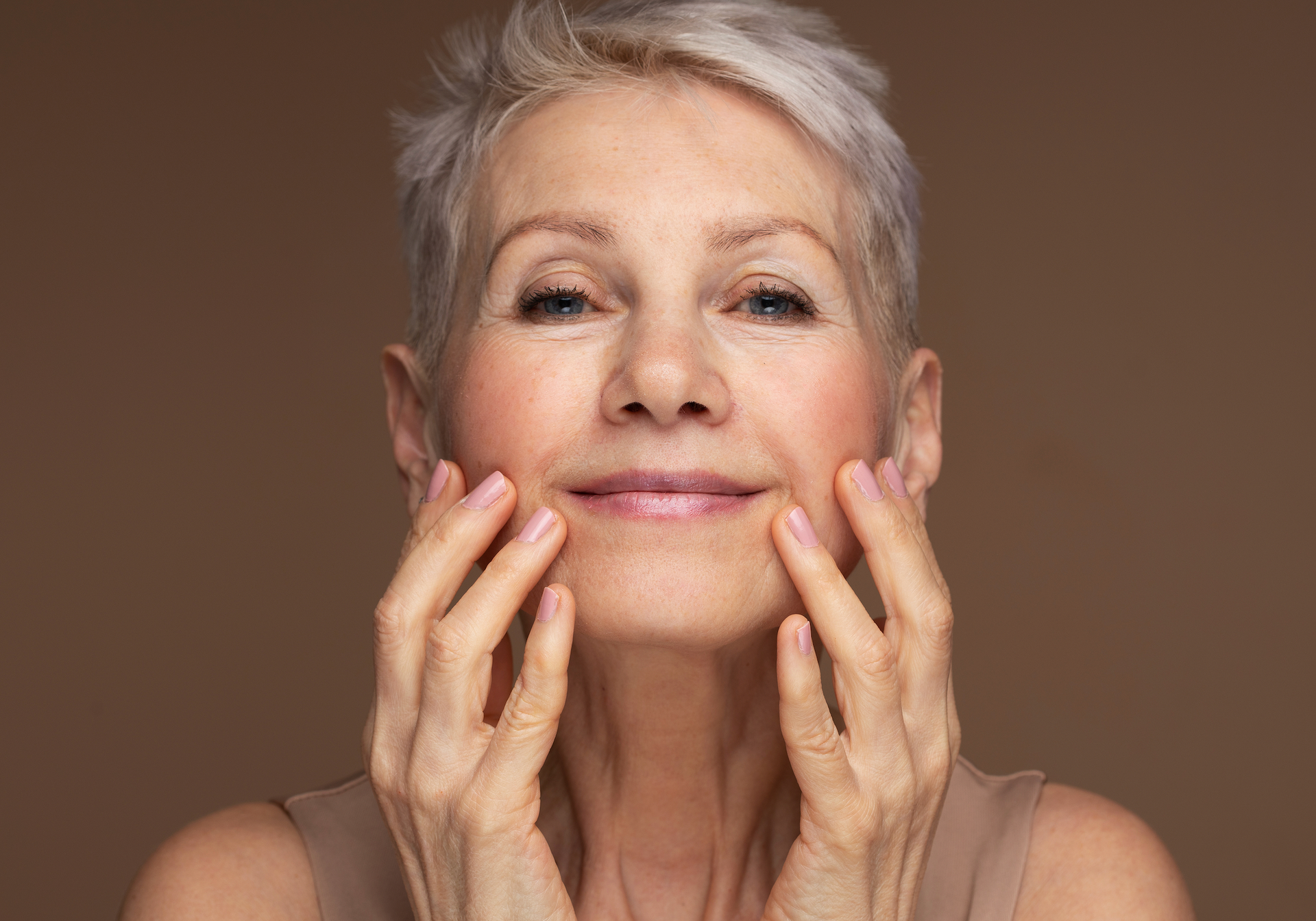 An Older Woman Is Touching Her Face With Her Hands And Smiling
