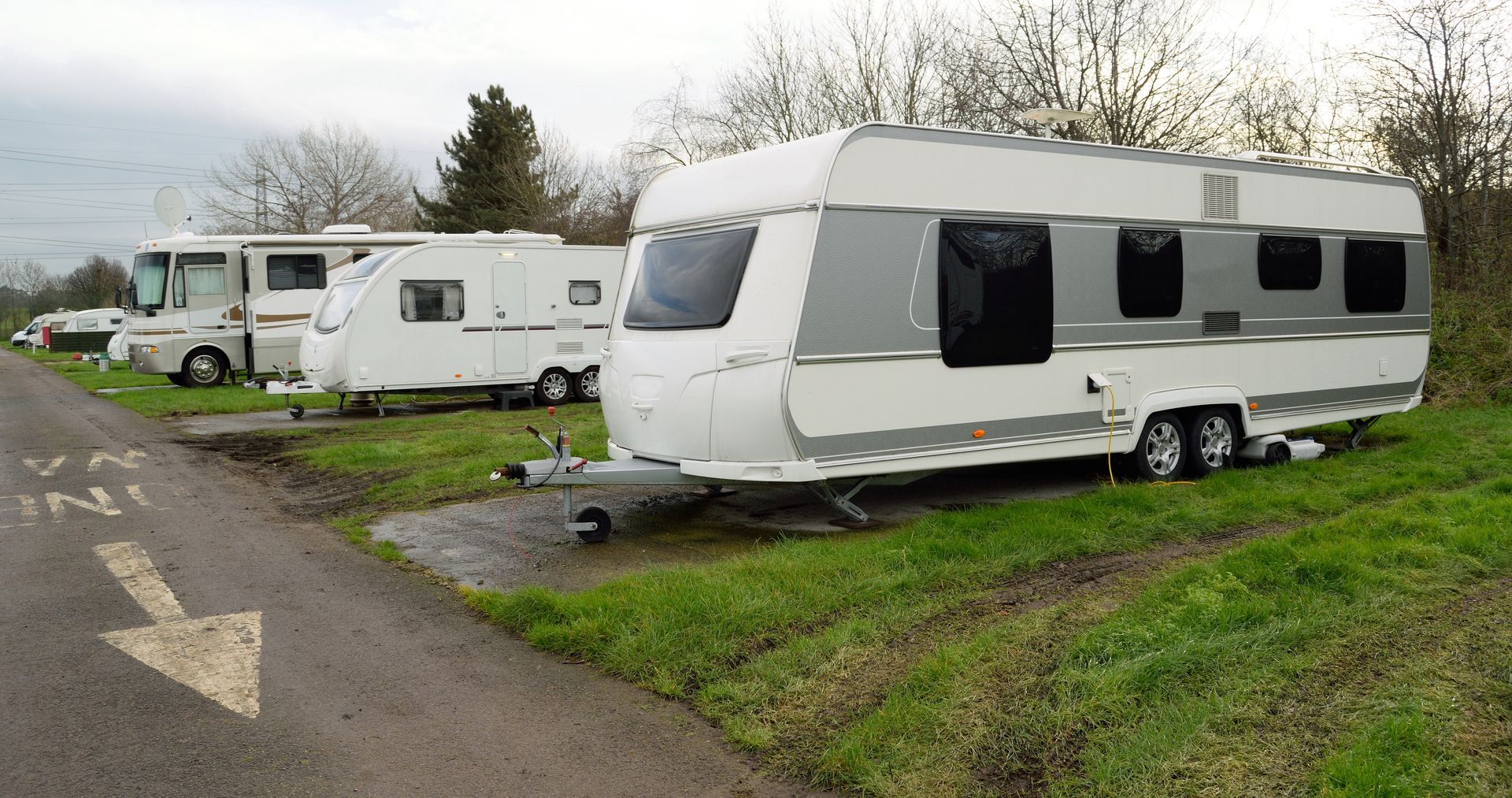 Several travel trailers and a motorhome parked on grassy spots along a paved path in an outdoor campground.