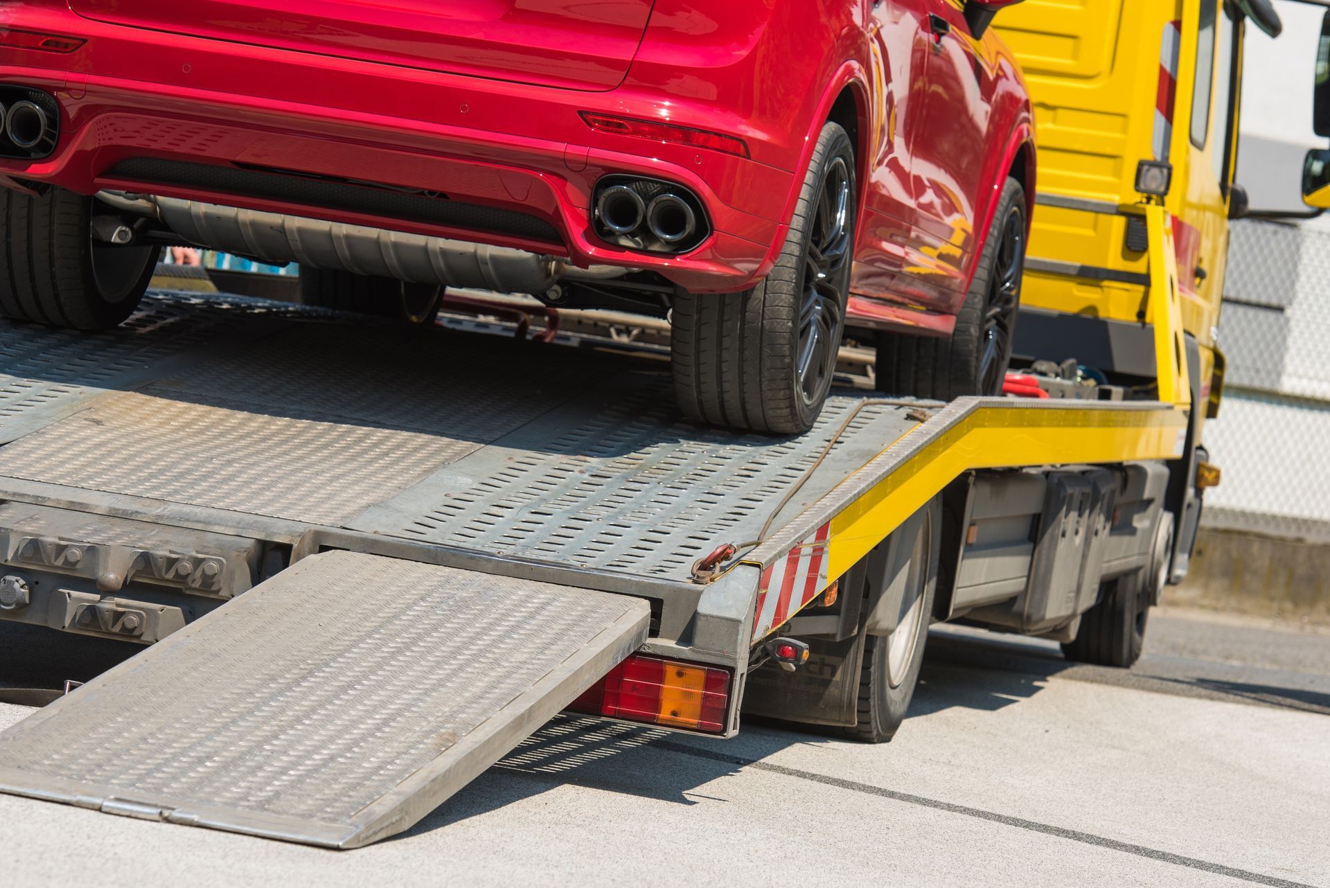 A red car is parked on the flatbed of a yellow tow truck with its loading ramp extended.