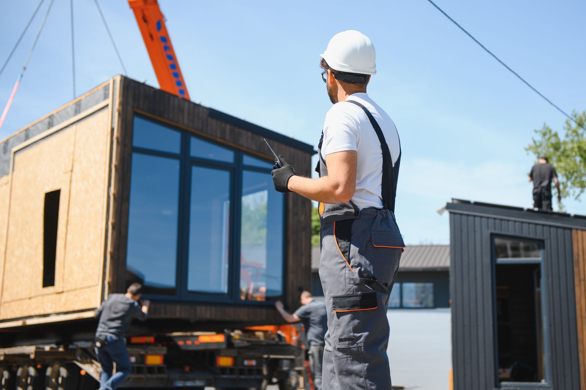 Workers at a sunny construction site use a crane to position a modular building unit.