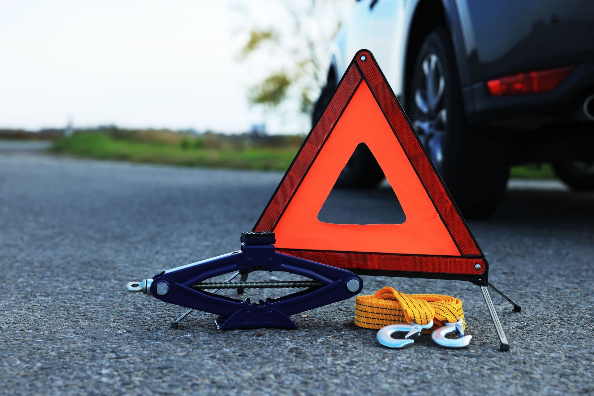 A breakdown triangle, car jack, and tow rope placed on the road in front of a parked car.