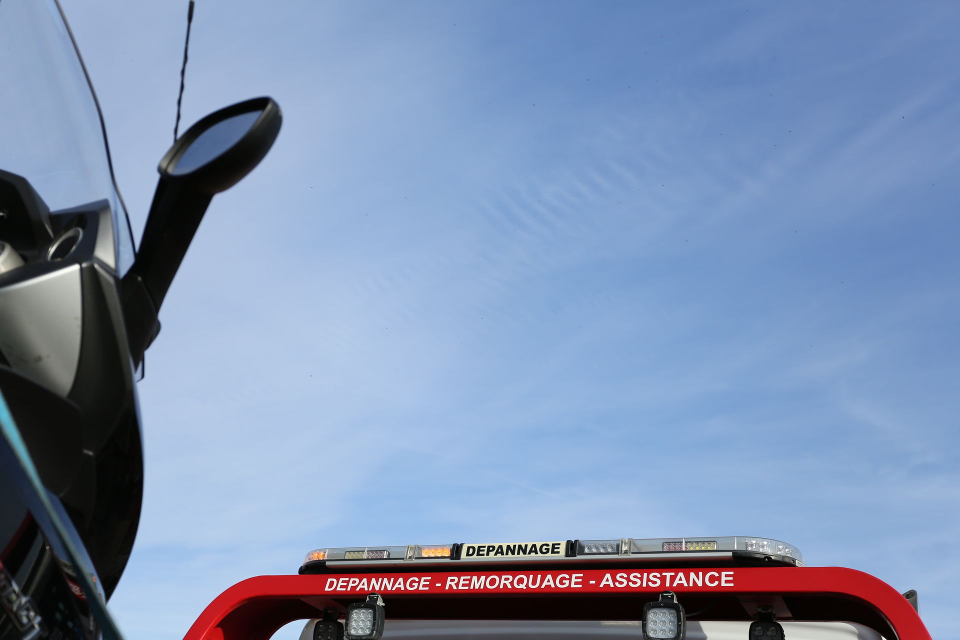 A close-up view of a red tow truck crane against a blue sky, displaying the text 