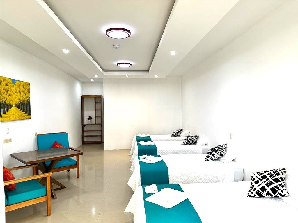Una habitación de hotel con tres camas, una mesa, sillas y un cuadro en la pared.