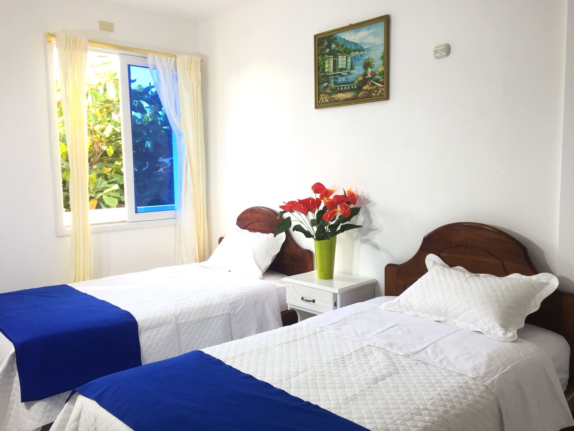 Un dormitorio con dos camas individuales y un jarrón de flores en la mesita de noche.