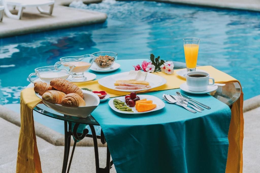 Una mesa con platos de comida y bebidas junto a una piscina.