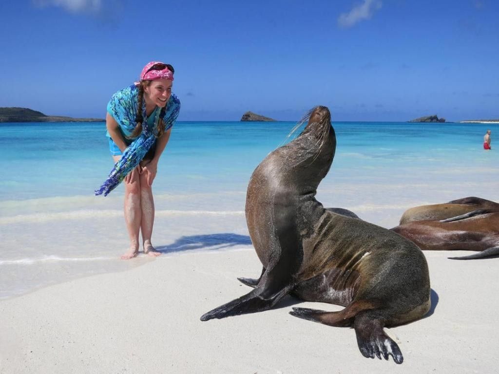 Una mujer parada junto a una foca en una playa