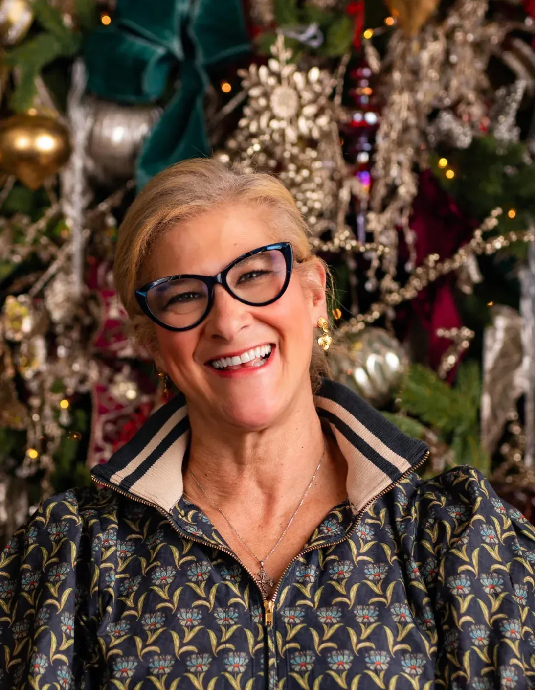 Woman wearing glasses smiles in front of a Christmas tree with decorations.