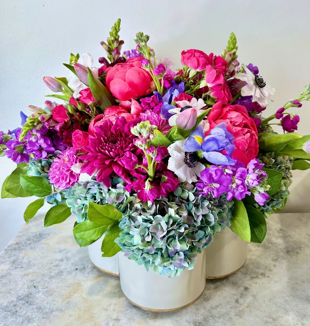 Colorful floral arrangement in white vases; pink, purple, and blue flowers.