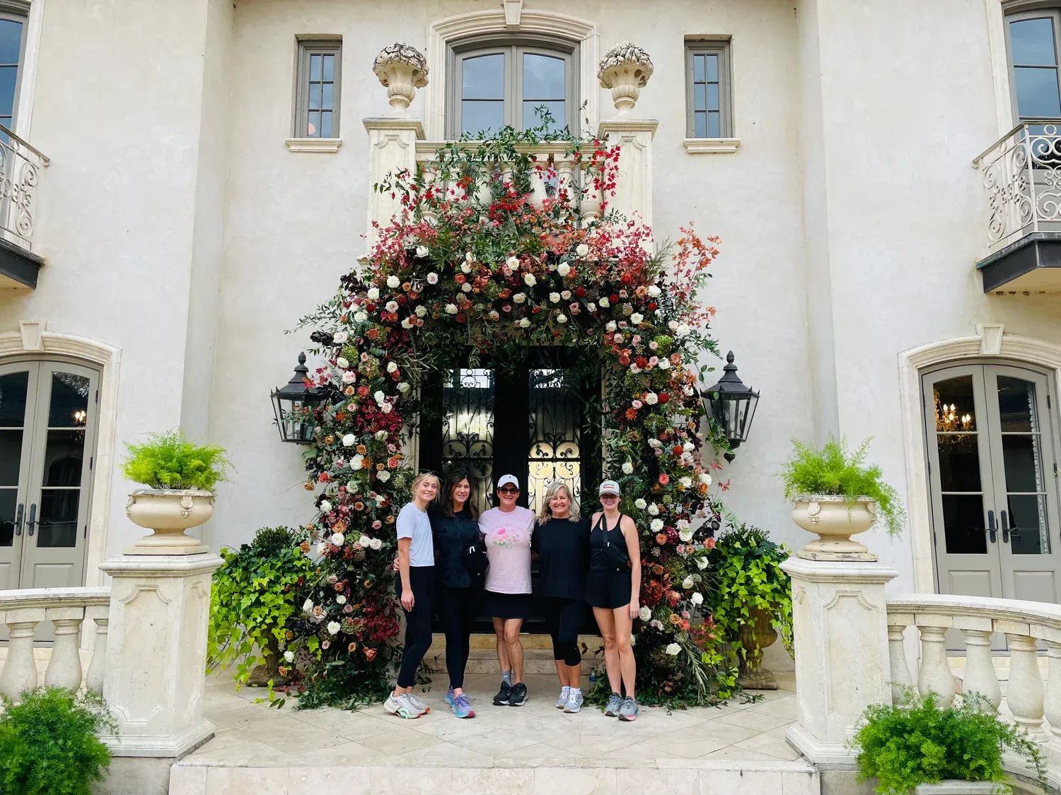 Group of women in front of a house with a floral archway.