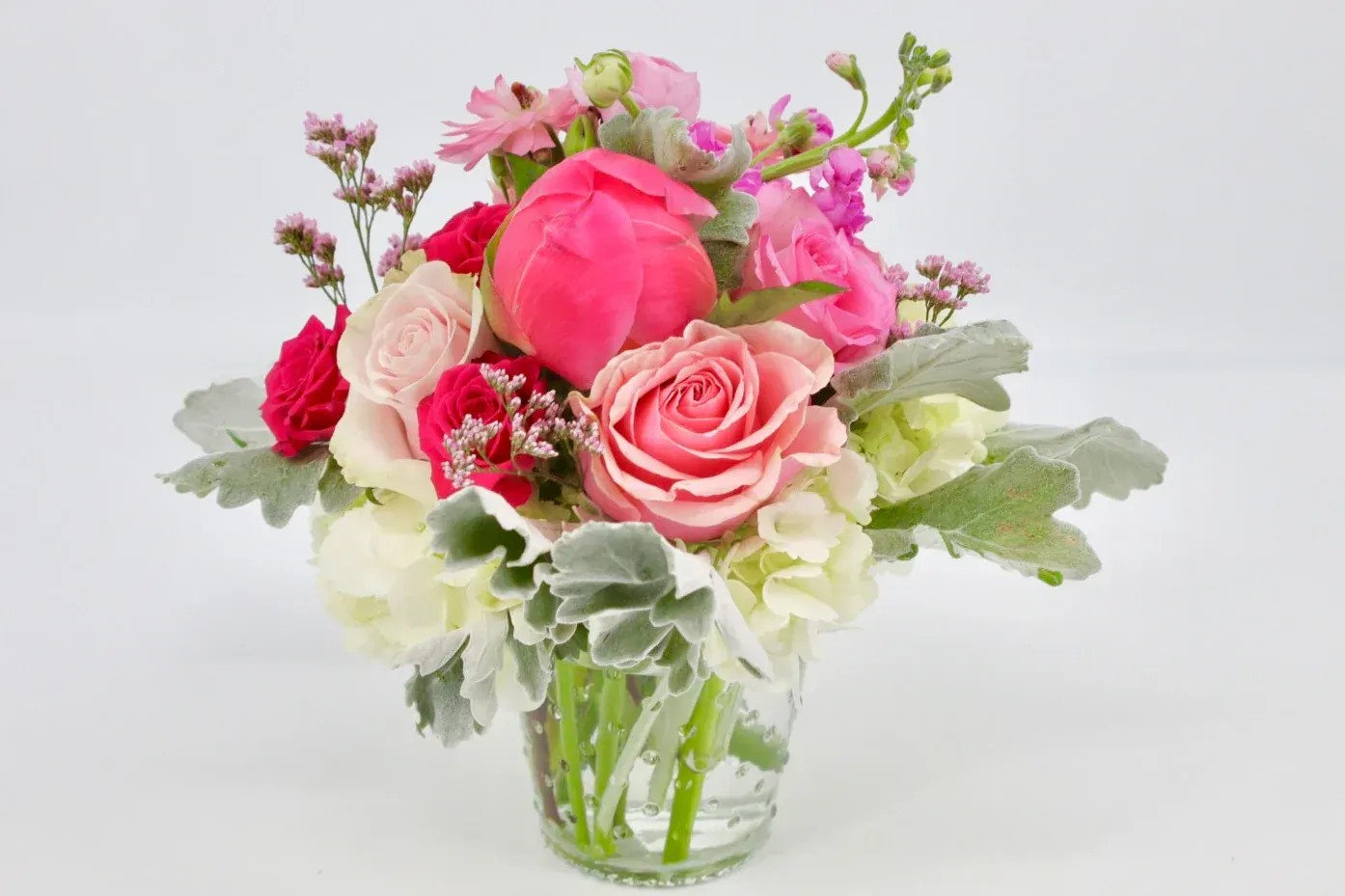 Vibrant pink and white flowers, including roses and peonies, in a clear glass vase.