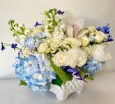Arrangement of blue and white flowers in a white, quilted ceramic vase.