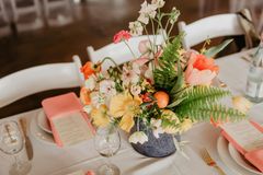 Floral centerpiece with coral and yellow blooms, on a table set with menus, plates, and glasses.