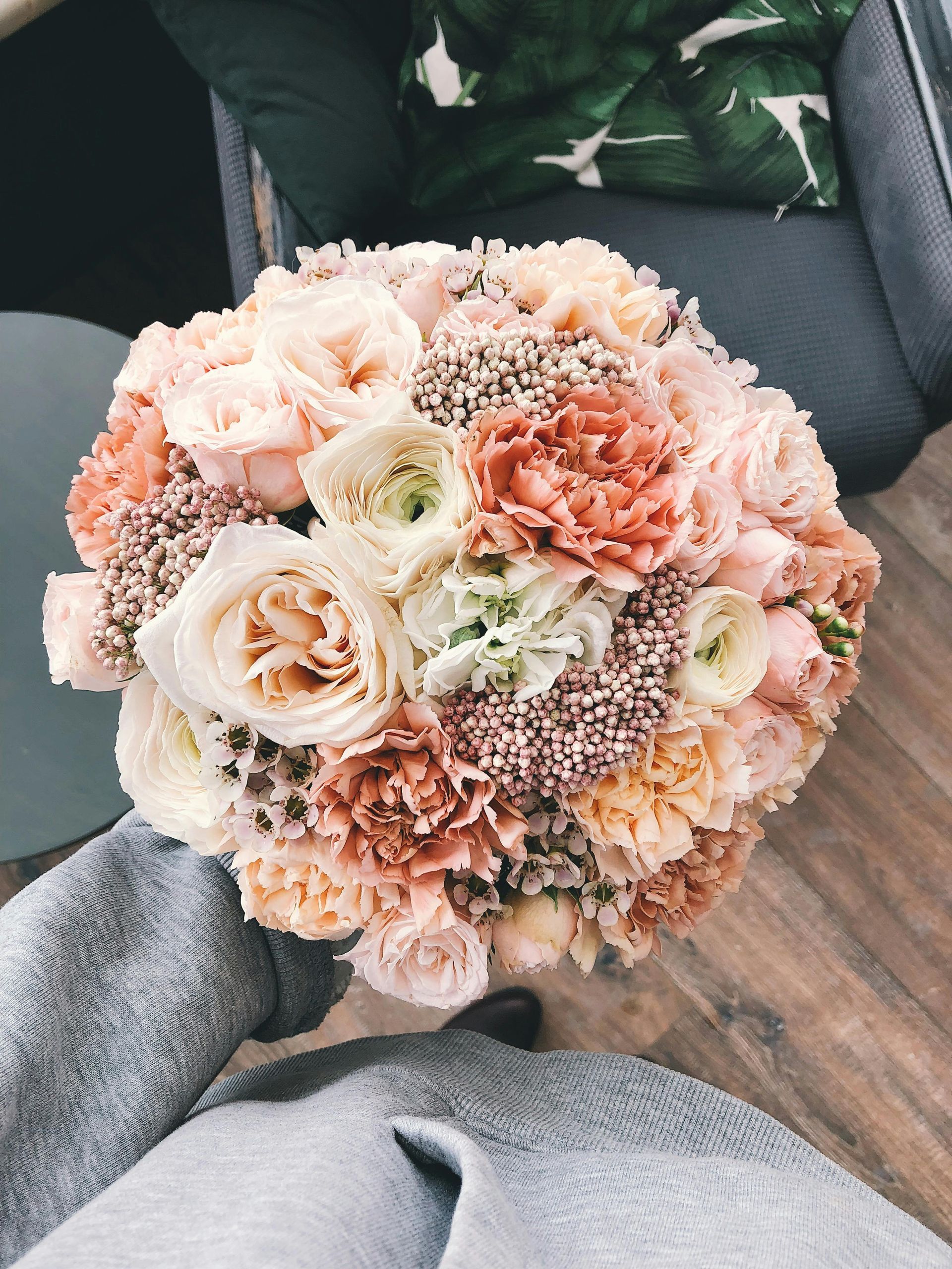 Bouquet of soft pink, peach, and cream flowers, held by someone in a gray sweater.