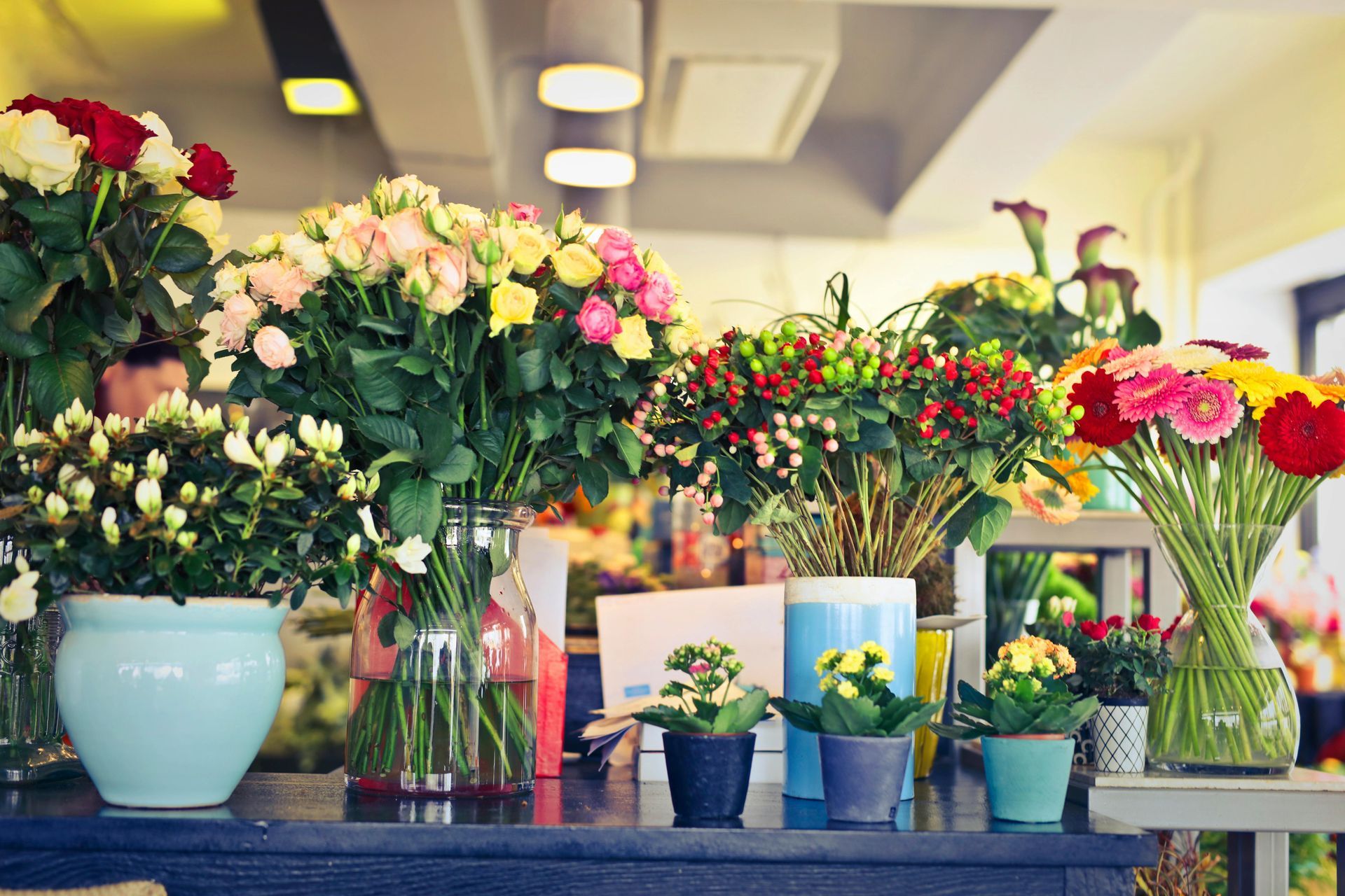 Flowers in vases and pots on a shop counter, in various colors and arrangements, with overhead lights.