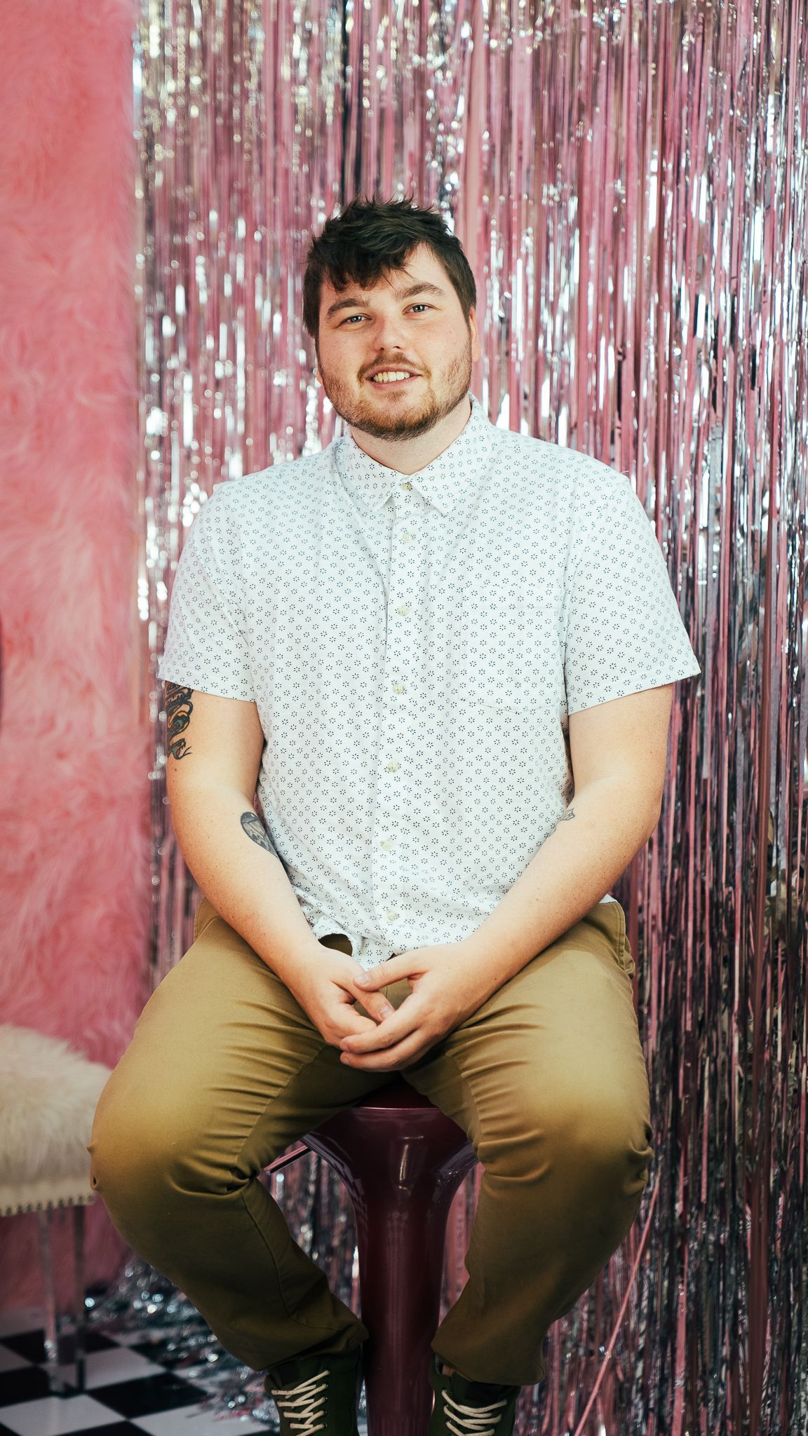 A man is sitting on a bar stool in front of a pink curtain.