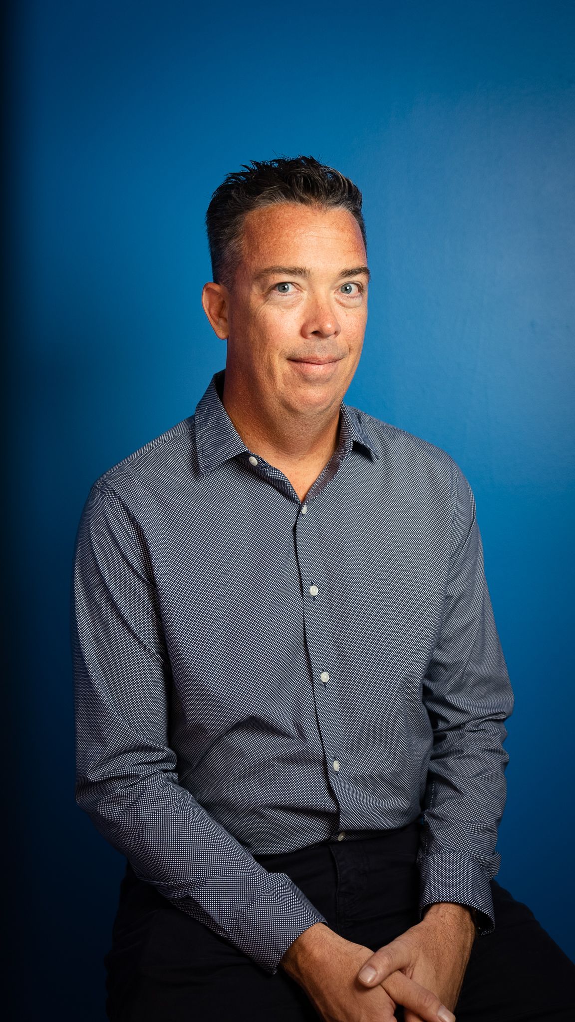 A man in a plaid shirt is sitting in front of a blue wall.