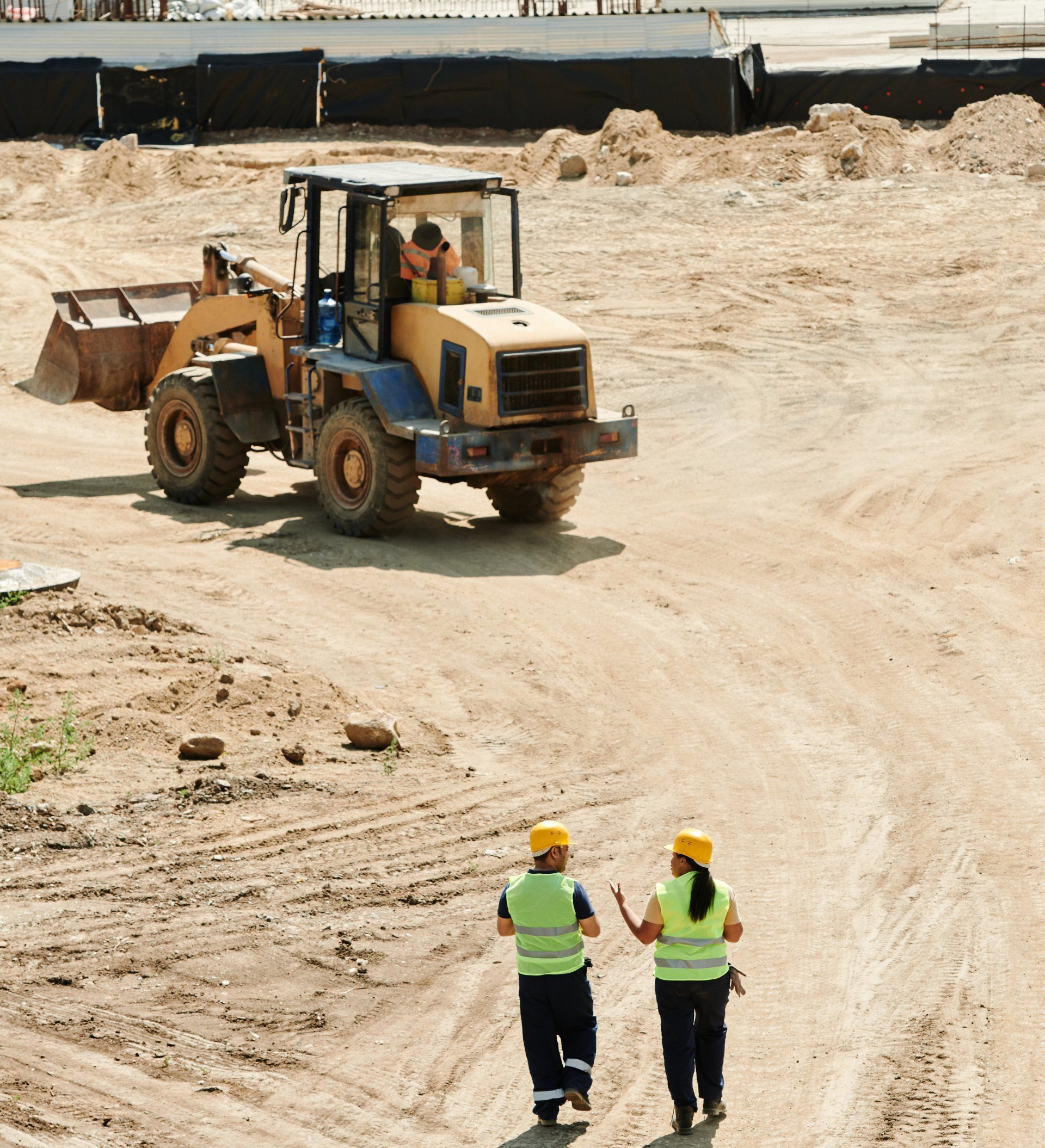 Construction Site: Workers in Vests and Hard Hats Walk Toward a Yellow Bulldozer — Des’s Driving School in Callala Bay, NSW