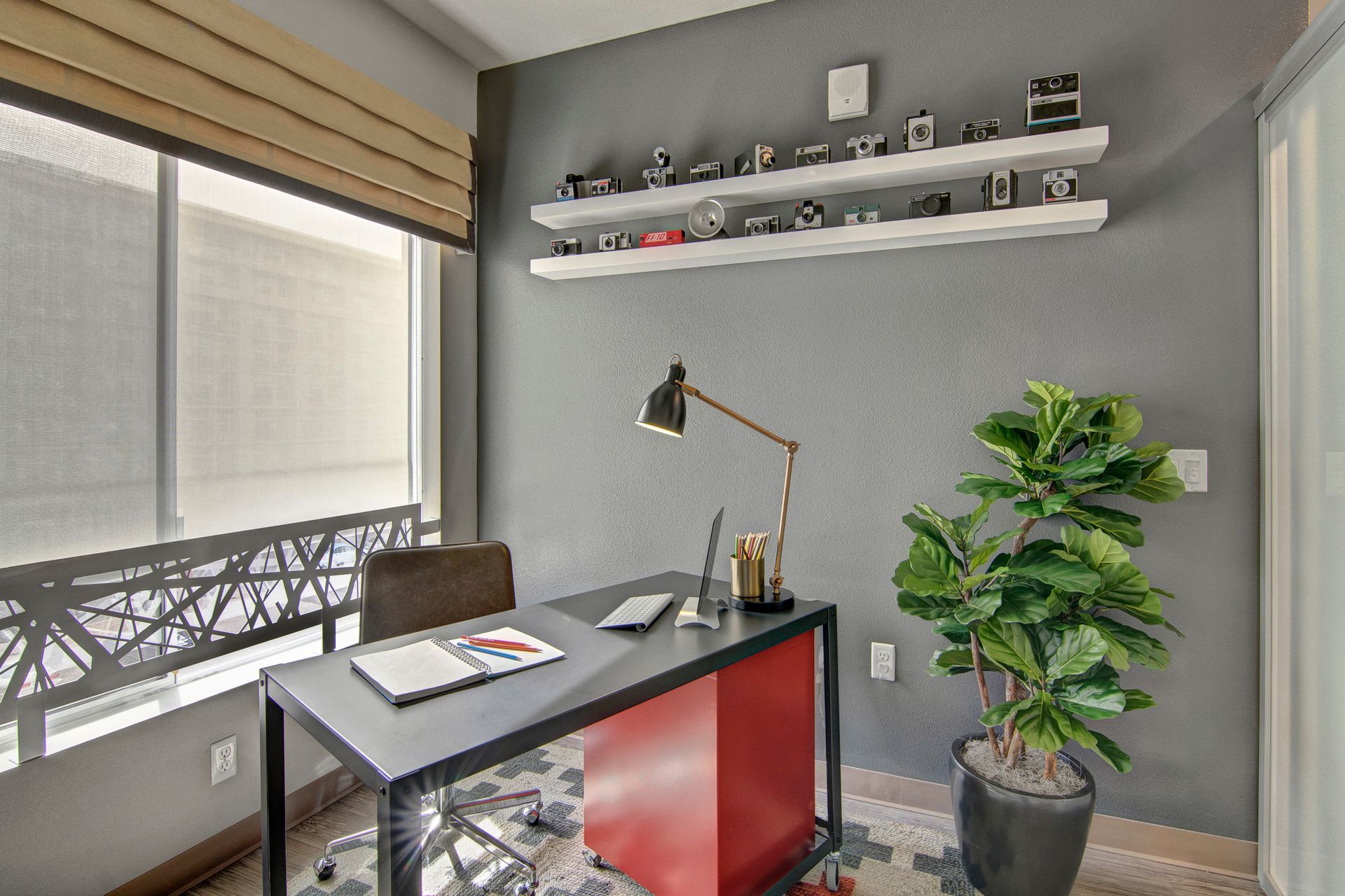 A home office with a desk , chair , lamp and potted plant.