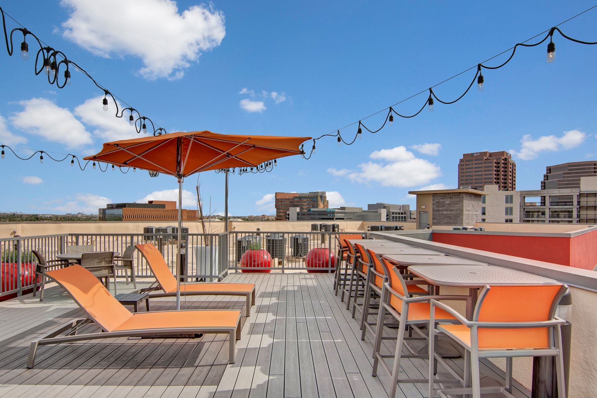 A rooftop deck with tables and chairs and an orange umbrella.