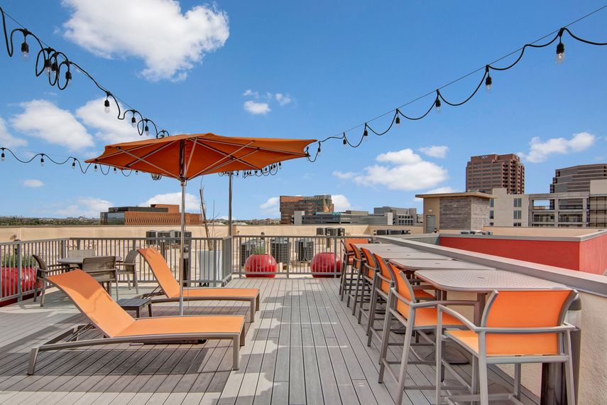 A rooftop deck with tables and chairs and an orange umbrella.