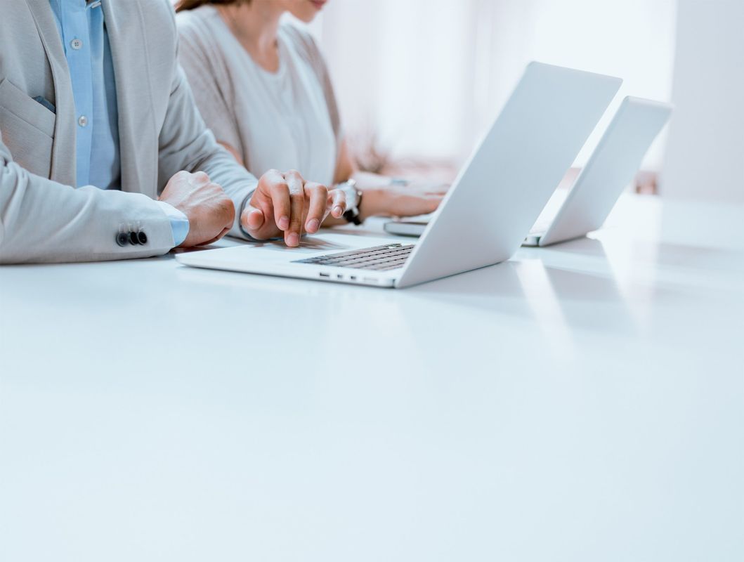 People working on laptops at a white table in an office.