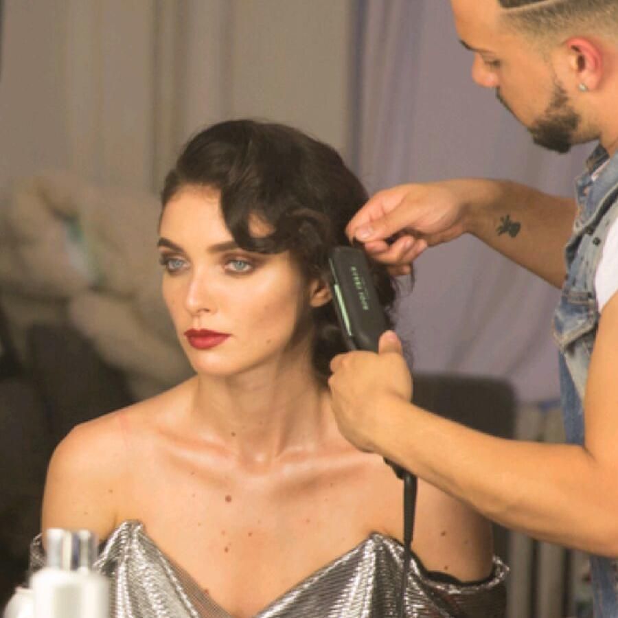 Woman with red lipstick has her hair styled by a man with a hair straightener. In a salon.