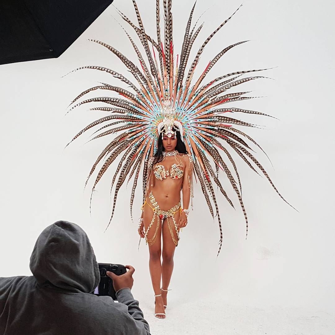 Woman in elaborate feathered costume poses for photographer in studio.