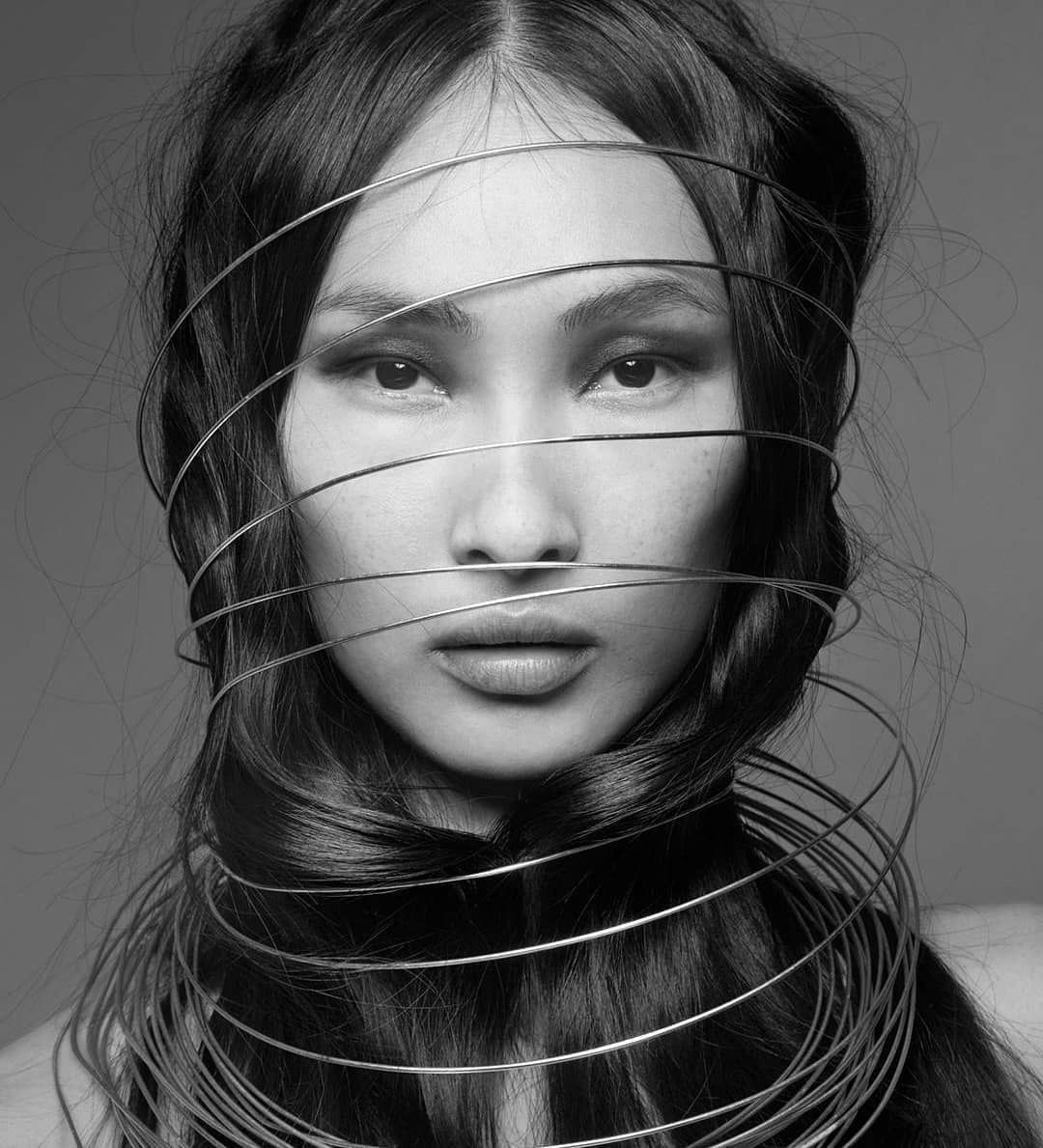 Monochrome portrait of a woman with metallic wires wrapped around her head and neck, gazing directly forward.