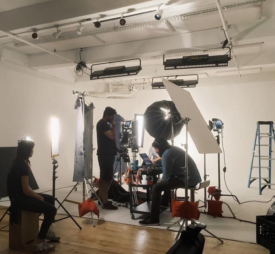 Film crew in a studio setting; adjusting lights and equipment, preparing to film.