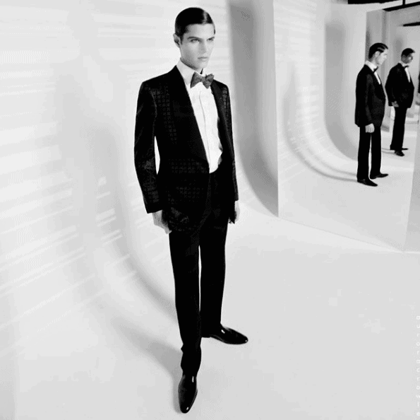 Man in a tuxedo poses in a studio with his reflections. Black and white.
