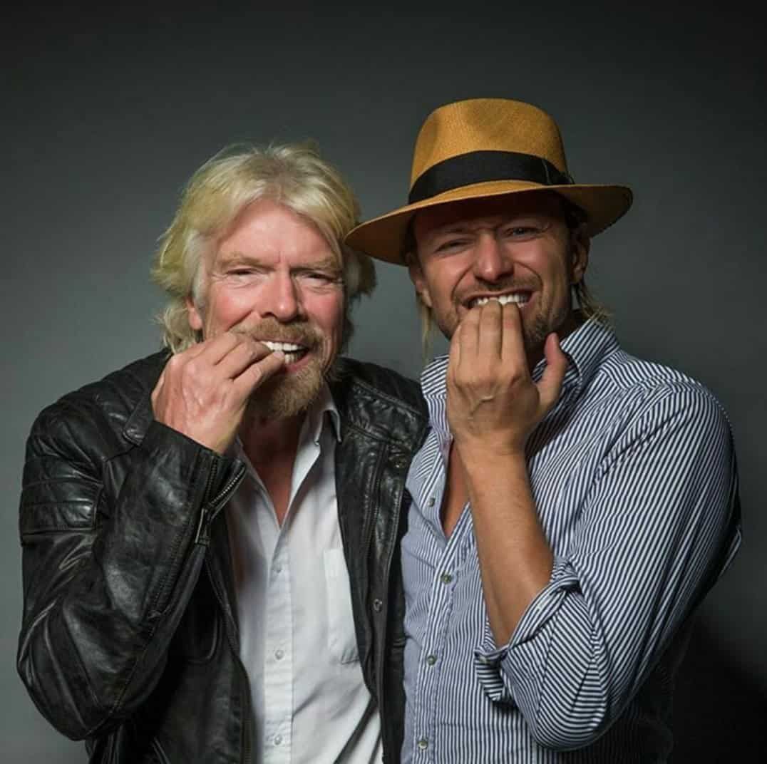 Richard Branson and another man smiling, holding up teeth whitening strips.